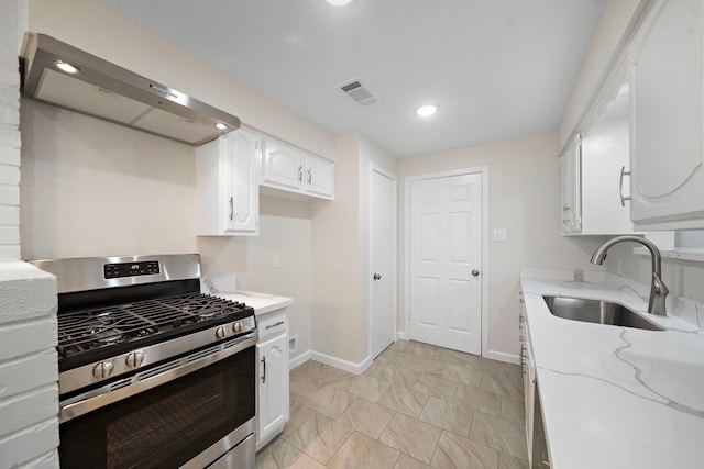 kitchen featuring visible vents, white cabinets, stainless steel range with gas stovetop, a sink, and wall chimney range hood