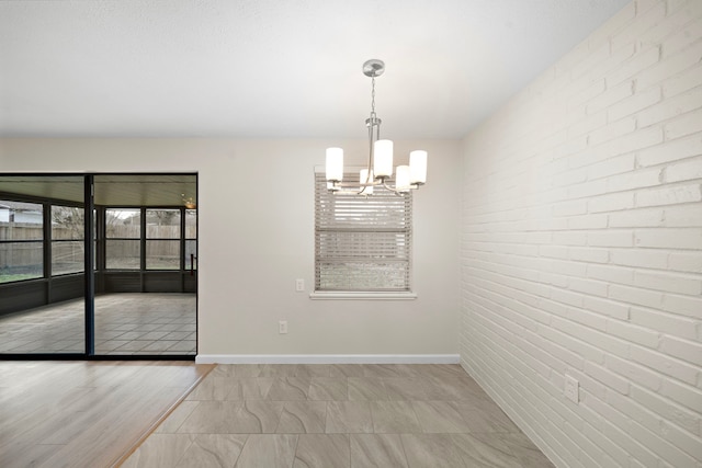 unfurnished dining area featuring baseboards, brick wall, and an inviting chandelier