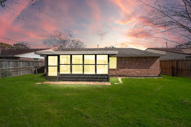 back of property at dusk with a yard, brick siding, and a fenced backyard