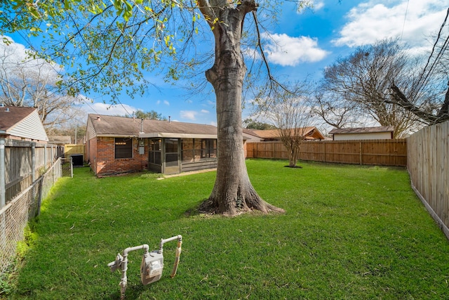 back of property with a sunroom, brick siding, a yard, and a fenced backyard