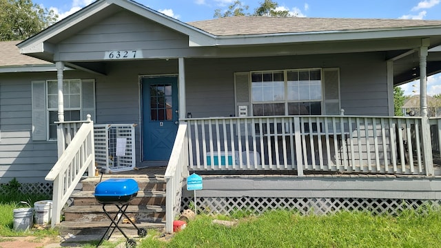 doorway to property with a porch and roof with shingles