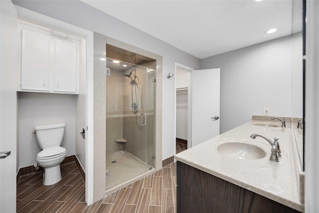 full bath featuring double vanity, toilet, wood tiled floor, a sink, and a shower stall