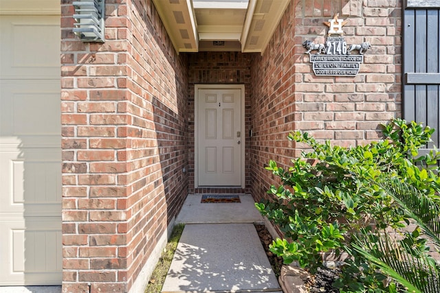 view of exterior entry with a garage and brick siding