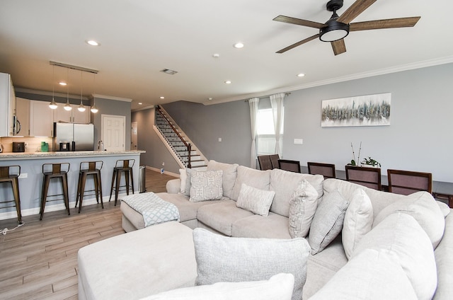 living area featuring crown molding, light wood-style flooring, ceiling fan, recessed lighting, and stairs
