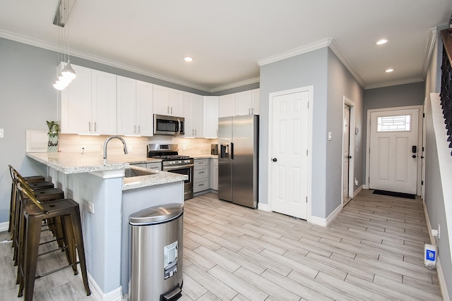 kitchen featuring light stone counters, a sink, appliances with stainless steel finishes, baseboards, and a peninsula