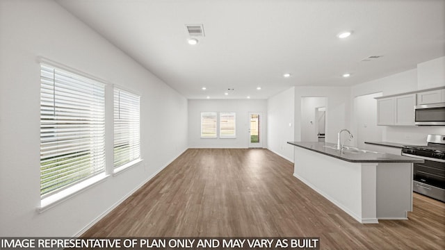 kitchen featuring visible vents, an island with sink, appliances with stainless steel finishes, wood finished floors, and a sink