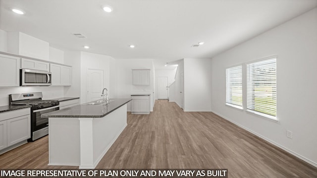 kitchen with a center island with sink, visible vents, appliances with stainless steel finishes, a sink, and dark stone countertops