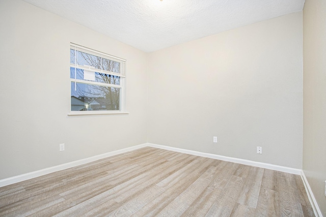 spare room with light wood-type flooring, baseboards, and a textured ceiling