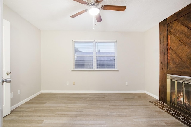 unfurnished living room with ceiling fan, a fireplace with flush hearth, light wood-style flooring, and baseboards