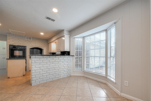 kitchen featuring white cabinets, dark countertops, a peninsula, black oven, and light tile patterned flooring