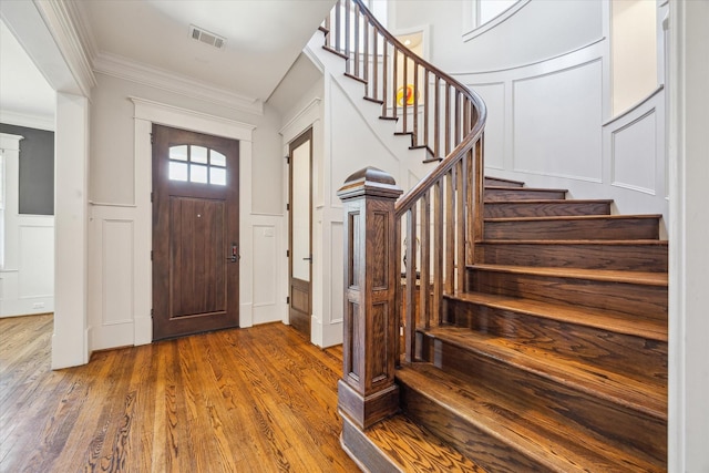 entryway with visible vents, a decorative wall, crown molding, and wood finished floors