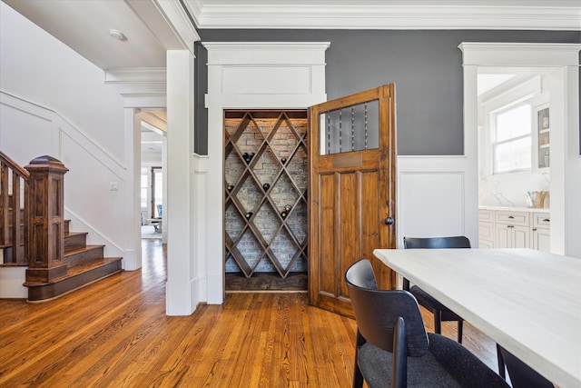 interior space featuring wainscoting, a decorative wall, crown molding, and wood finished floors