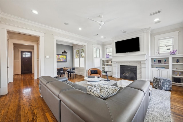 living area featuring crown molding, recessed lighting, visible vents, a brick fireplace, and wood finished floors