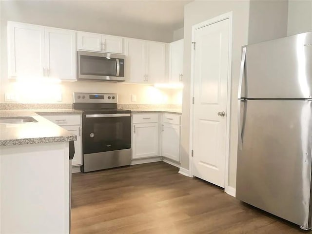 kitchen featuring white cabinets, dark wood-style floors, stainless steel appliances, light countertops, and a sink