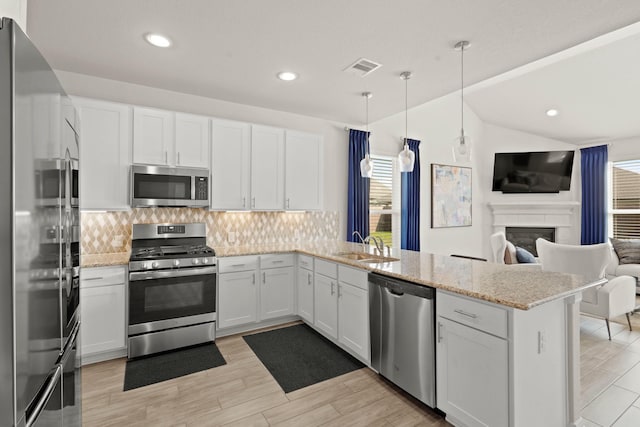 kitchen featuring stainless steel appliances, hanging light fixtures, open floor plan, white cabinetry, and a peninsula