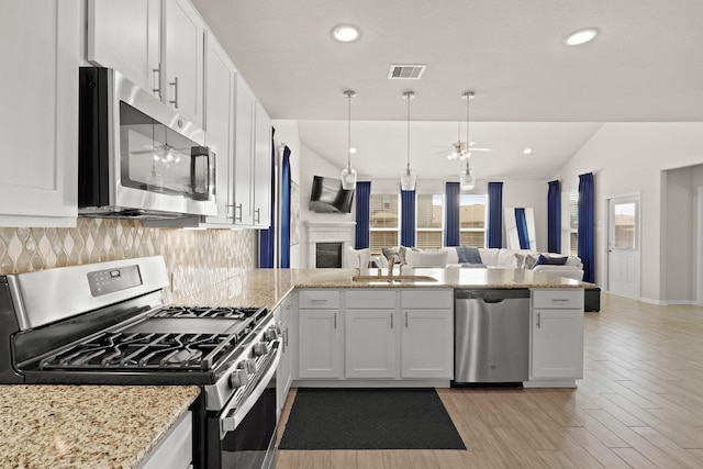 kitchen featuring stainless steel appliances, open floor plan, white cabinetry, a sink, and a peninsula