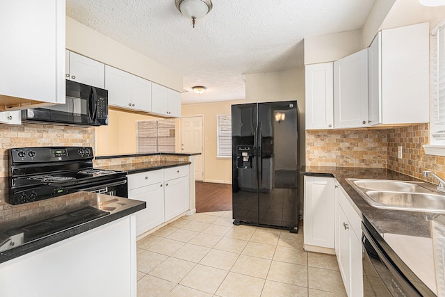 kitchen with black appliances, dark countertops, a sink, and white cabinetry