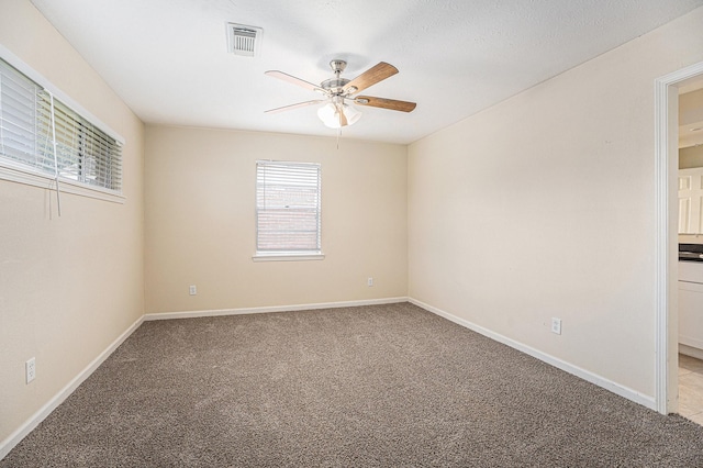 empty room featuring baseboards, ceiling fan, visible vents, and light colored carpet