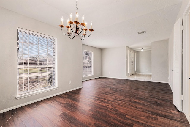 spare room featuring dark wood-style floors, visible vents, an inviting chandelier, a textured ceiling, and baseboards