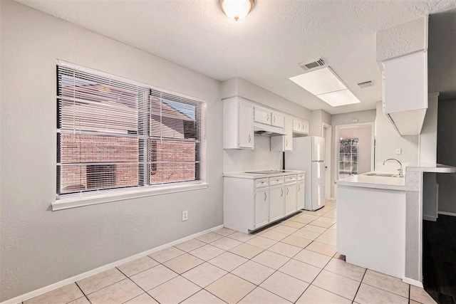 kitchen featuring white cabinets, black electric cooktop, light countertops, and freestanding refrigerator