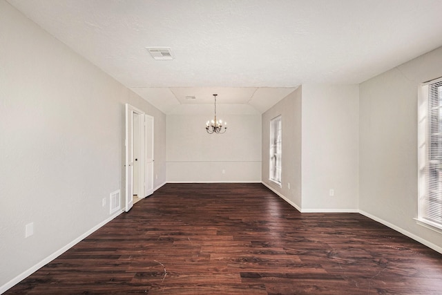 unfurnished room with dark wood-style floors, visible vents, a notable chandelier, and baseboards