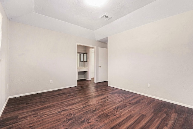 empty room featuring visible vents, baseboards, dark wood-style floors, vaulted ceiling, and a textured ceiling
