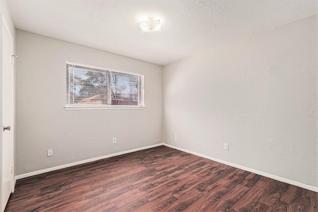 unfurnished room featuring dark wood-type flooring, a textured wall, a textured ceiling, and baseboards