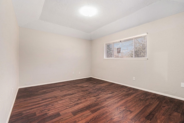 empty room featuring vaulted ceiling, a raised ceiling, dark wood finished floors, and baseboards