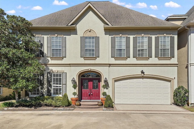 view of front of house featuring roof with shingles, driveway, and stucco siding