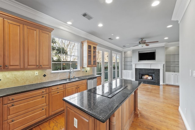 kitchen featuring a warm lit fireplace, a center island, a sink, light wood-style floors, and stainless steel dishwasher