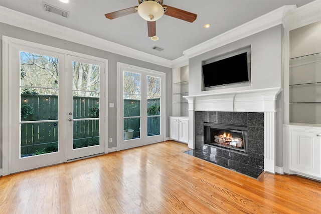 unfurnished living room featuring wood finished floors, visible vents, built in features, ornamental molding, and a tiled fireplace