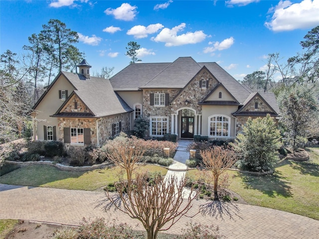 french country home with stone siding, a front lawn, french doors, and stucco siding