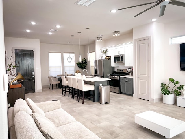 kitchen with a kitchen island with sink, stainless steel appliances, a kitchen breakfast bar, white cabinets, and light countertops