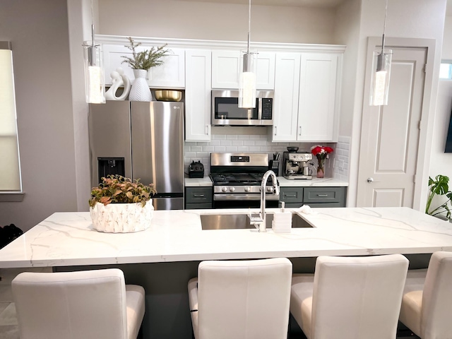 kitchen featuring white cabinets, an island with sink, appliances with stainless steel finishes, a breakfast bar area, and pendant lighting