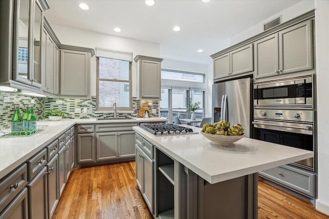 kitchen featuring tasteful backsplash, stainless steel appliances, light countertops, gray cabinetry, and a sink