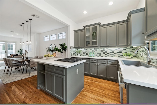 kitchen featuring a sink, light countertops, gray cabinets, a center island, and pendant lighting