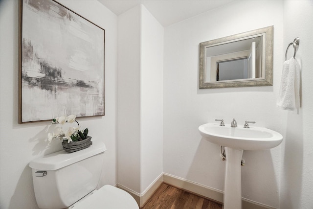 half bath featuring a sink, toilet, baseboards, and wood finished floors