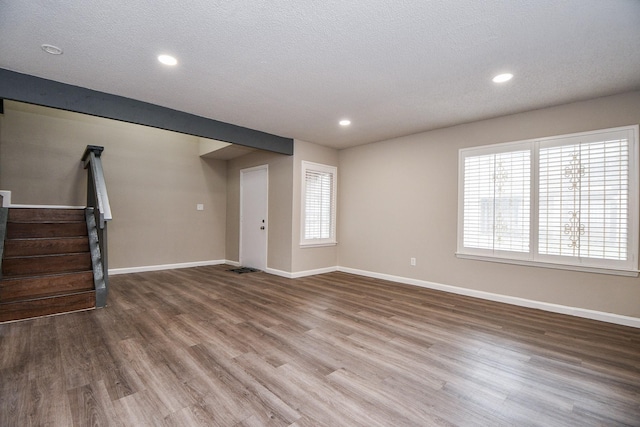 unfurnished living room featuring a textured ceiling, stairway, wood finished floors, and baseboards