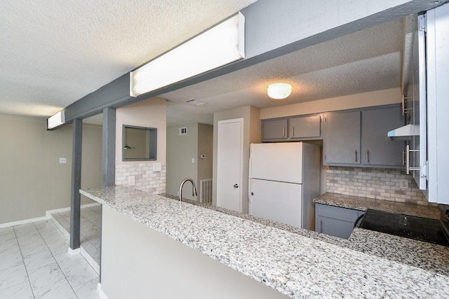 kitchen featuring a peninsula, marble finish floor, light stone counters, and freestanding refrigerator