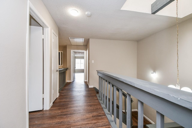 hallway with attic access, dark wood-type flooring, a textured ceiling, and baseboards