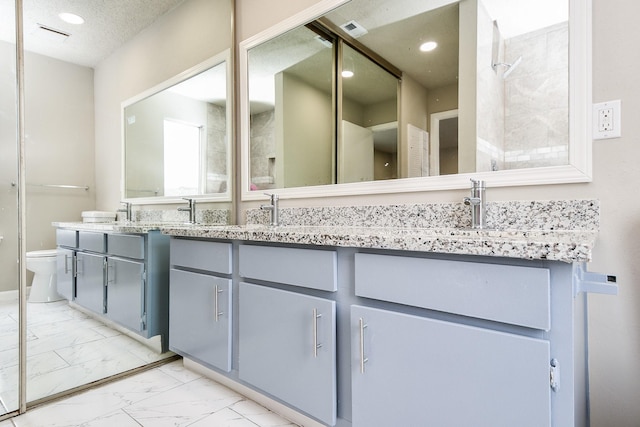 full bathroom featuring marble finish floor, double vanity, toilet, a sink, and a textured ceiling