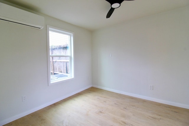 empty room featuring light wood-type flooring, a wall mounted air conditioner, and baseboards