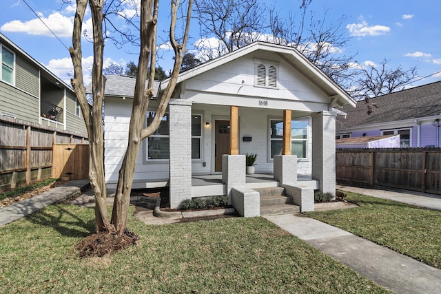 view of front of home with covered porch, a front yard, and fence