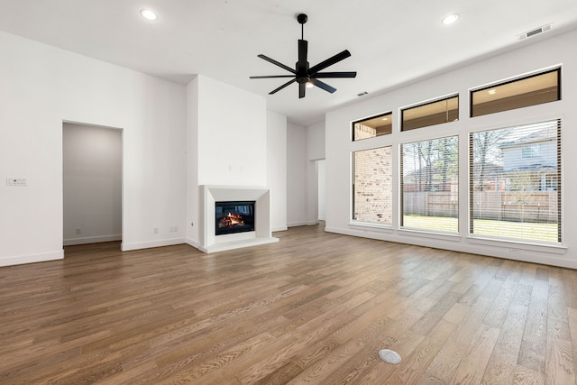 unfurnished living room featuring visible vents, a ceiling fan, a glass covered fireplace, wood finished floors, and recessed lighting