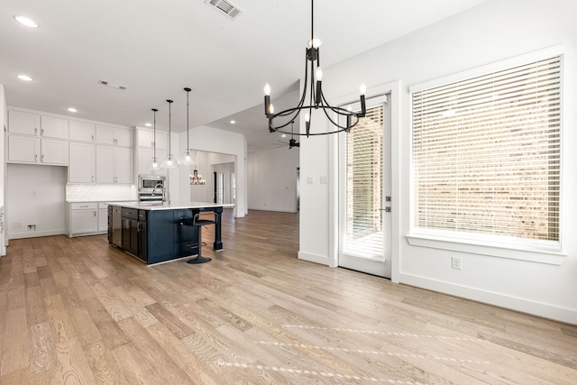 kitchen with pendant lighting, a notable chandelier, light countertops, white cabinetry, and an island with sink