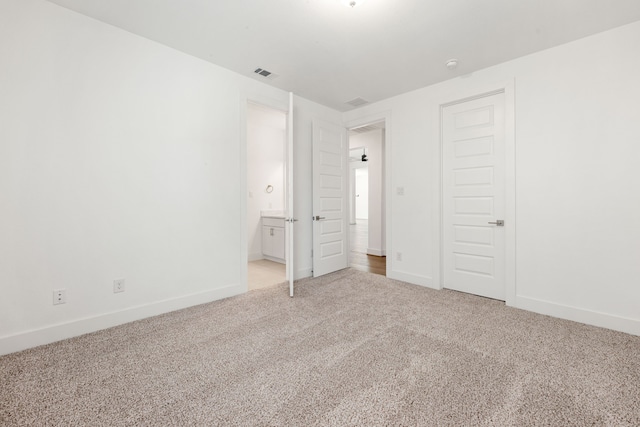 unfurnished bedroom with baseboards, ensuite bathroom, visible vents, and light colored carpet