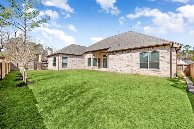 back of house featuring a fenced backyard, a lawn, brick siding, and roof with shingles