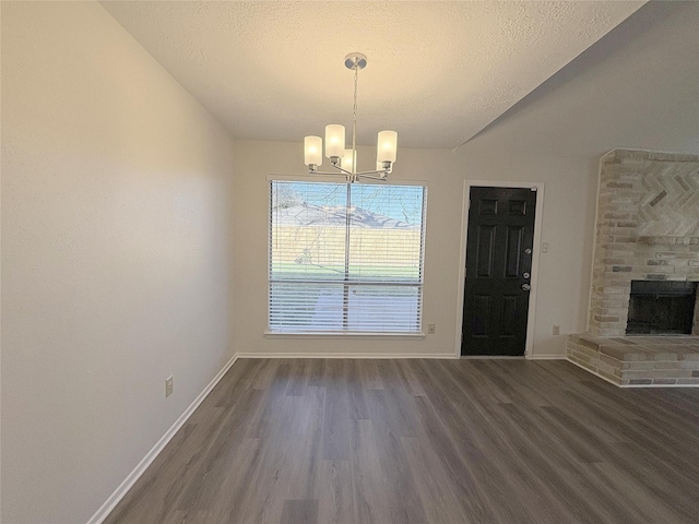 unfurnished dining area featuring dark wood-style floors, a brick fireplace, baseboards, and an inviting chandelier