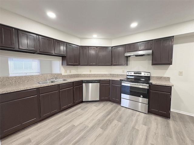 kitchen featuring light wood finished floors, appliances with stainless steel finishes, a sink, dark brown cabinets, and under cabinet range hood