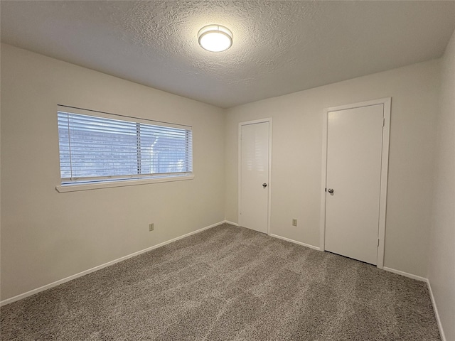 unfurnished bedroom featuring carpet flooring, a textured ceiling, and baseboards